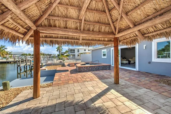 View of patio / terrace with a gazebo, a boat dock, an in ground hot tub, and a water view