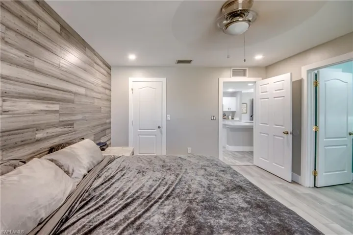 Bedroom with wood walls, a ceiling fan, light wood-type flooring, an accent wall, and ensuite bath