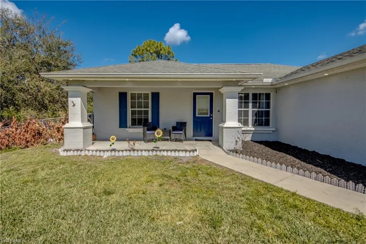 Property entrance featuring a lawn, covered porch, stucco siding, and roof with shingles