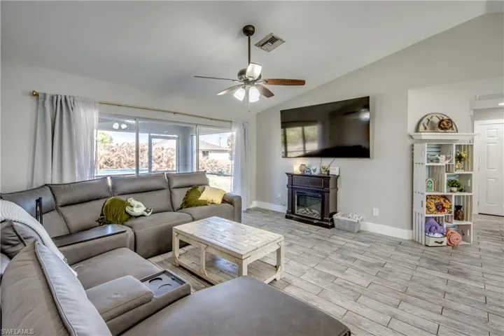 Living area with wood tiled floors, lofted ceiling, ceiling fan, and a glass covered fireplace