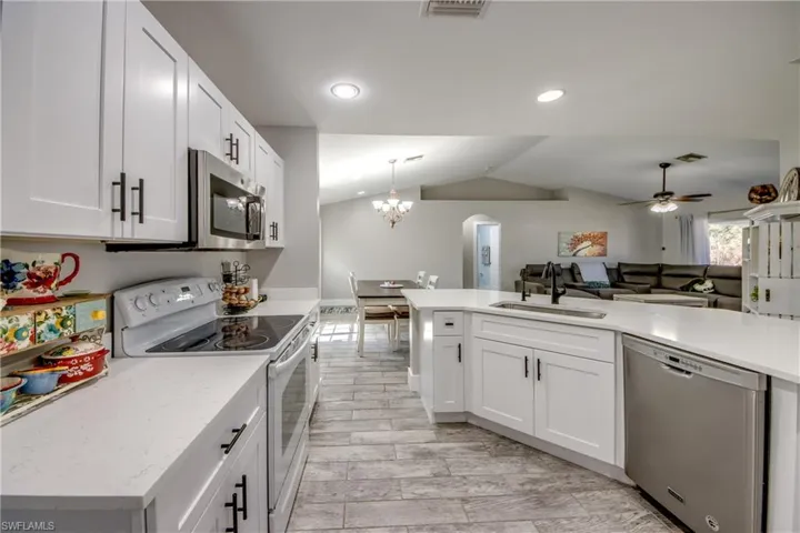 Kitchen with stainless steel appliances, open floor plan, white cabinets, wood tiled floors, and vaulted ceiling