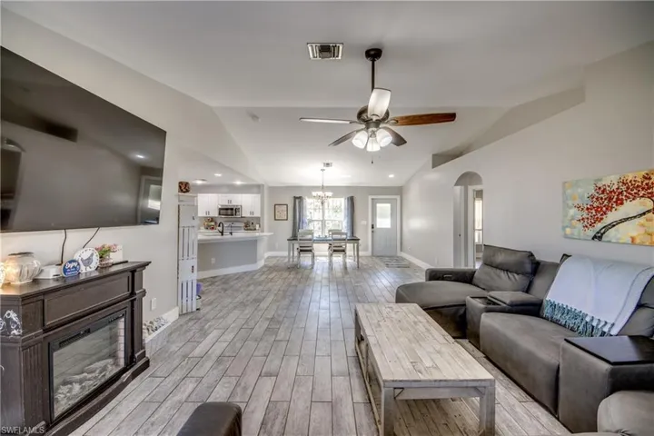 Living area featuring ceiling fan, wood finish floors, a glass covered fireplace, vaulted ceiling, and a chandelier