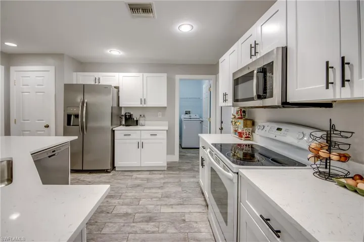 Kitchen with stainless steel appliances, white cabinetry, washer / clothes dryer, and light stone countertops