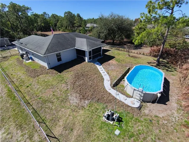 Outdoor pool featuring view of scattered trees, a sunroom, and a lawn