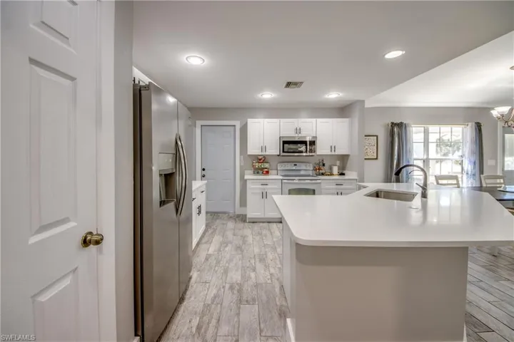 Kitchen with stainless steel appliances, white cabinetry, wood finish floors, an island with sink, and light stone counters