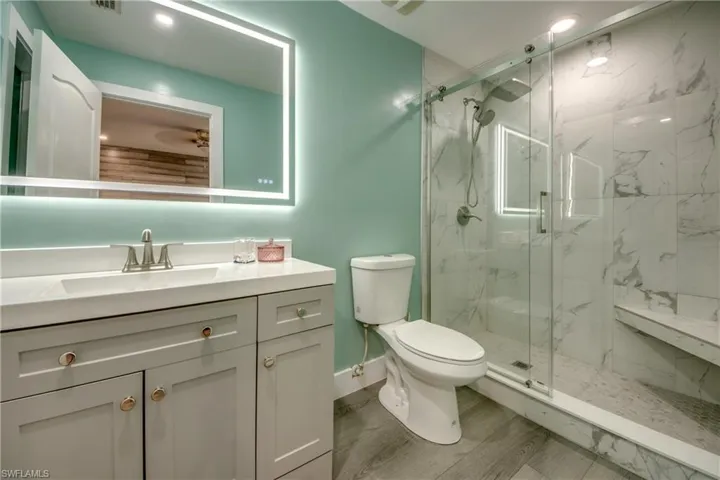 Bathroom featuring vanity, a marble finish shower, wood finished floors, and recessed lighting