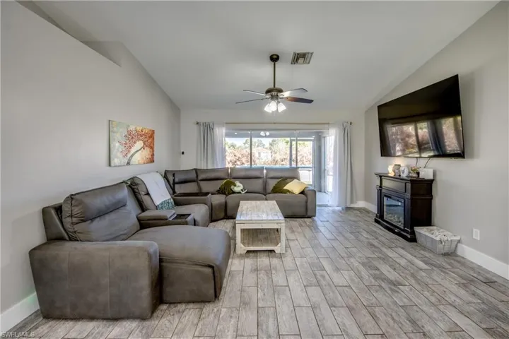 Living area with wood tiled floors, lofted ceiling, a ceiling fan, and a glass covered fireplace