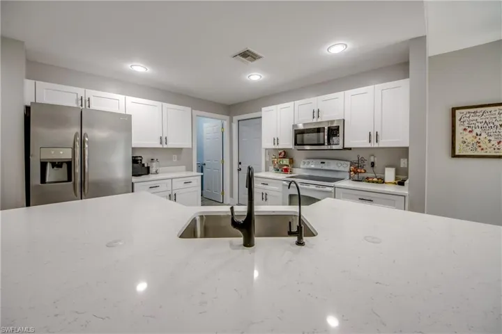 Kitchen with stainless steel appliances, white cabinets, and light stone counters