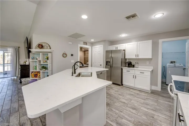 Kitchen with white cabinetry, stainless steel appliances, a center island with sink, wood tiled floors, and light stone counters