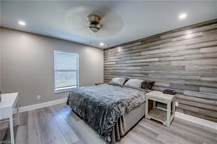 Bedroom with an accent wall, wood walls, light wood-style flooring, and ceiling fan