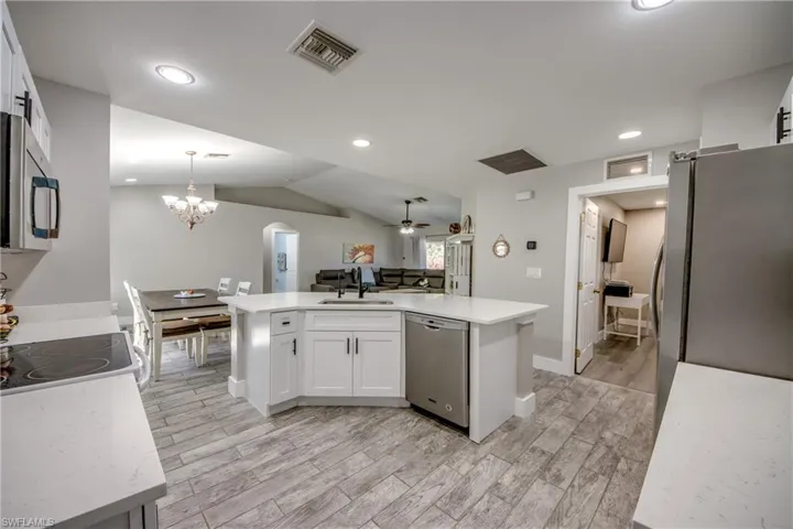Kitchen with white cabinets, wood finish floors, arched walkways, and lofted ceiling