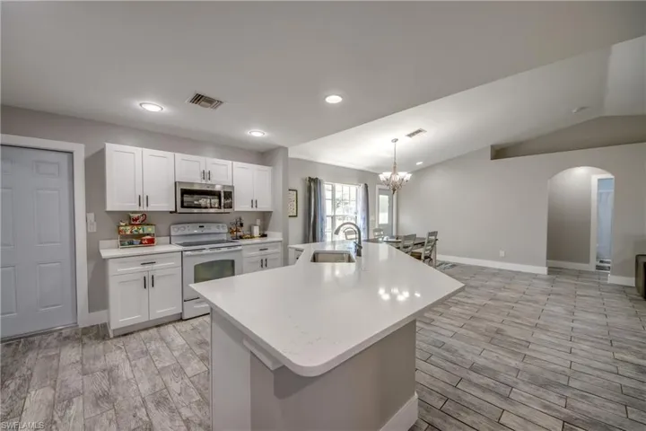 Kitchen featuring wood tiled floors, white range with electric cooktop, white cabinets, stainless steel microwave, and vaulted ceiling