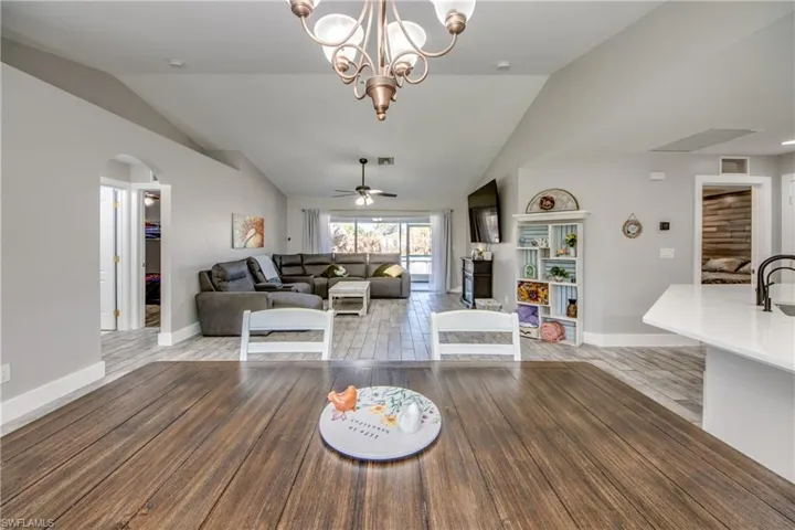 Living room with vaulted ceiling, a ceiling fan, arched walkways, light wood-style floors, and suspended lighting