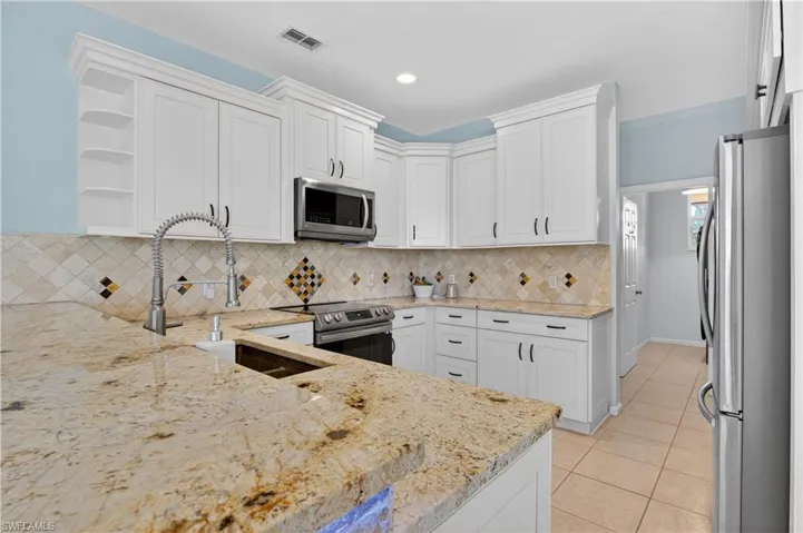 Kitchen with stainless steel appliances, open shelves, white cabinets, light stone countertops, and recessed lighting