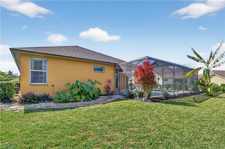 Back of house with a sunroom, a lanai, a yard, and stucco siding