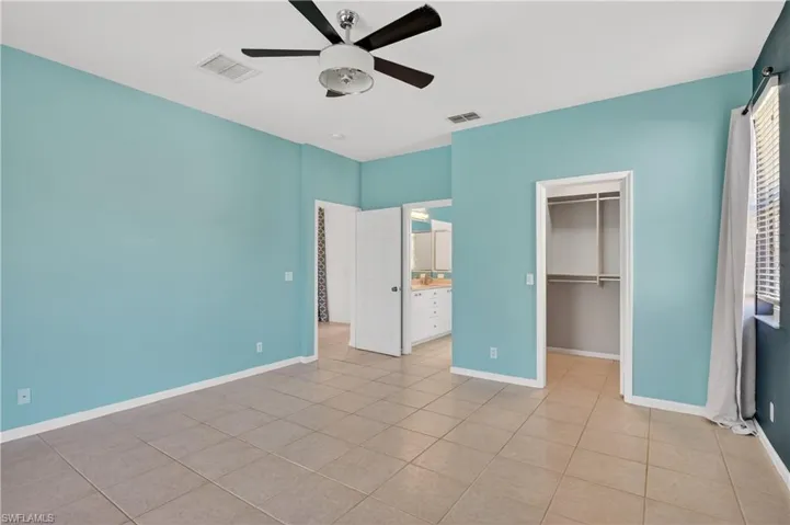 Master bedroom with a spacious closet, a ceiling fan, light tile patterned floors, and ensuite bathroom