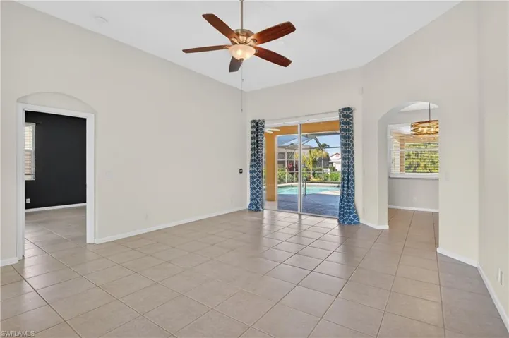 Unfurnished room with arched walkways, a ceiling fan, light tile patterned floors, a sunroom, and a high ceiling