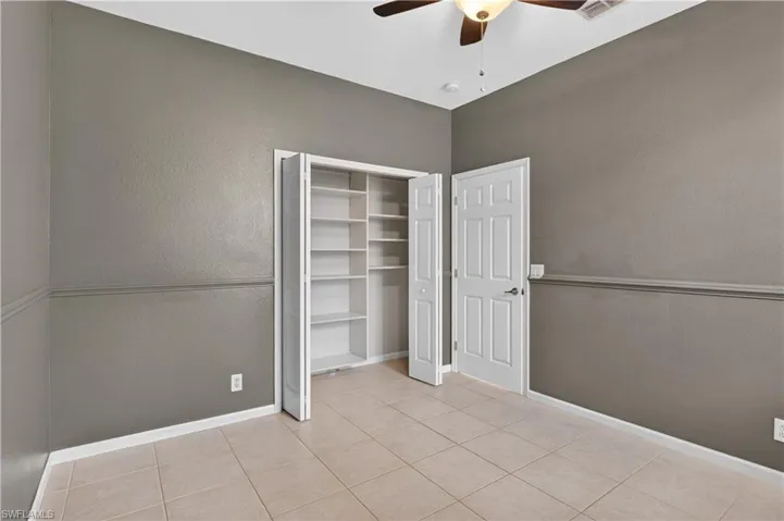 Unfurnished bedroom featuring a textured wall, ceiling fan, light tile patterned floors, and a closet