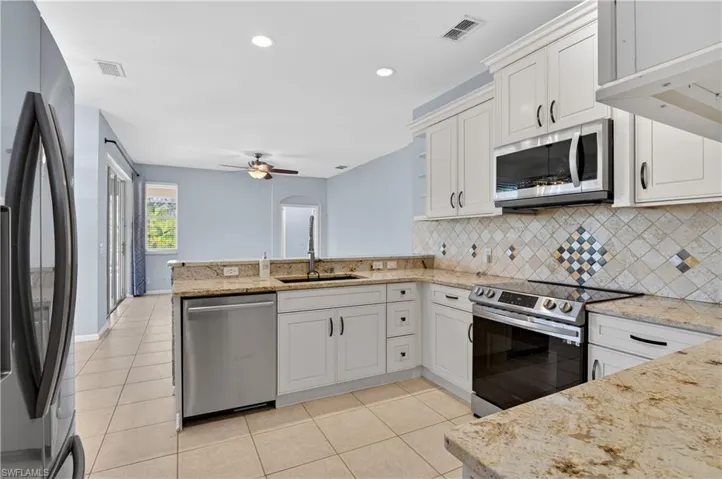 Kitchen with stainless steel appliances, light stone counters, a peninsula, light tile patterned floors, and decorative backsplash