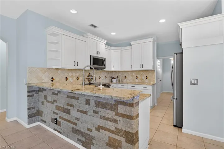 Kitchen with open shelves, a peninsula, light stone countertops, white cabinetry, and stainless steel appliances