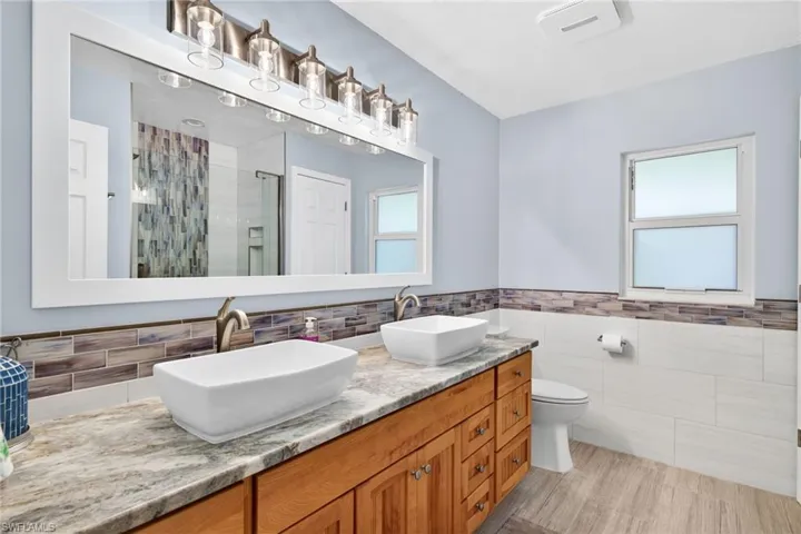 The updated guest bathroom provides warm cabinetry, dual vessel sinks with granite countertop and designer tile accents.