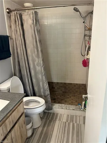 Bathroom featuring vanity, walk in shower, tile patterned flooring, and toilet