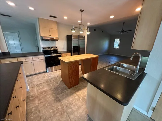 Kitchen with appliances with stainless steel finishes, under cabinet range hood, a center island, tasteful backsplash, and ceiling fan