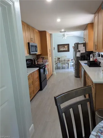 Kitchen with appliances with stainless steel finishes, ceiling fan, light tile patterned floors, and light stone counters