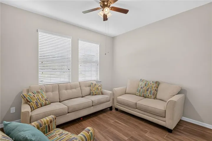 Bright room featuring two windows with horizontal blinds, wood-finish flooring, a ceiling fan with integrated lighting, and neutral wall tones