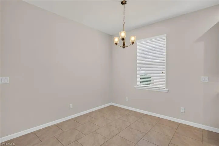Dining area featuring a bronze-finish chandelier with three lights, a window with white blinds, and light-toned tile flooring
