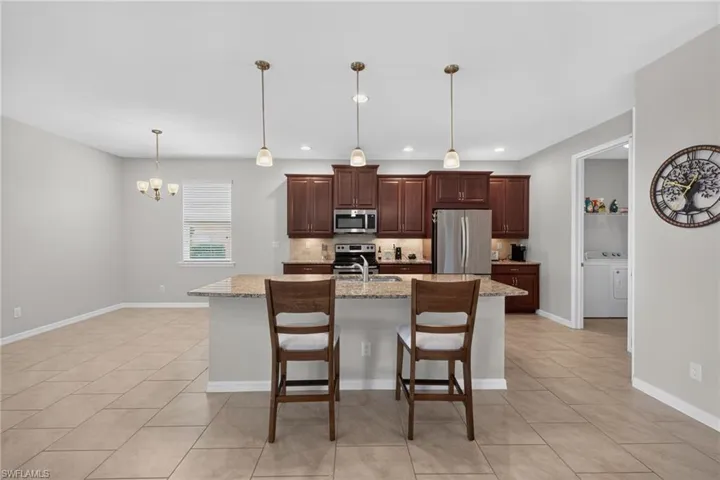 Open-concept kitchen featuring dark wood cabinetry, stainless steel appliances, and a central island with a granite-style countertop