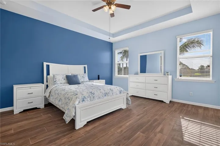Spacious room featuring wood-finish flooring, a tray ceiling with a ceiling fan, and two windows with horizontal blinds