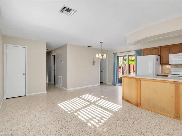 Open-concept living area featuring terrazzo flooring, a kitchen with wood cabinetry and a white countertop, and sliding glass doors providing access to the outdoors