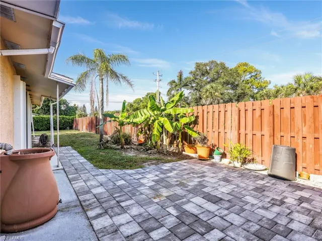Expansive backyard featuring a paver patio, a partial privacy fence, and mature trees including a palm and banana trees