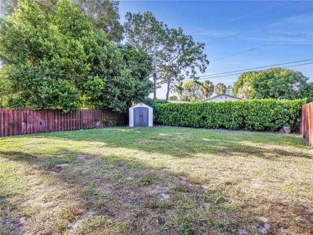 Spacious green yard featuring a storage shed, a wood fence, and mature perimeter landscaping