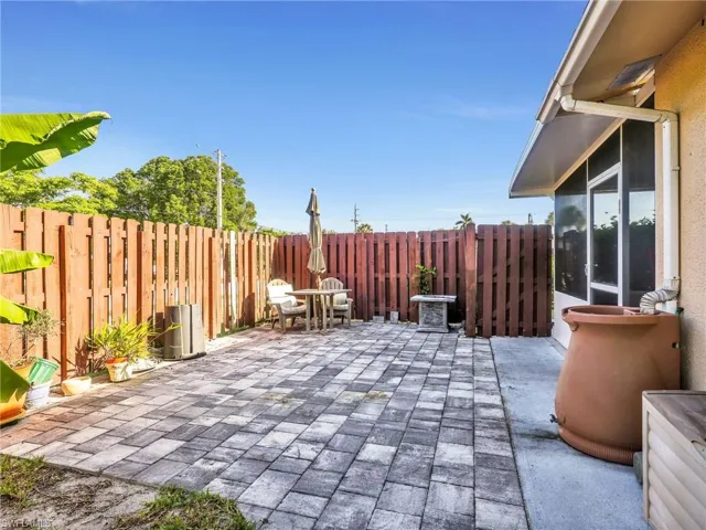 Spacious paved patio area featuring a privacy fence, screened enclosure, and a rain barrel system