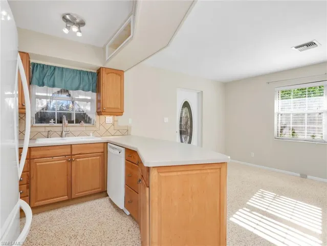 Kitchen featuring honey-toned wood cabinetry, a built-in dishwasher, and a light-toned countertop