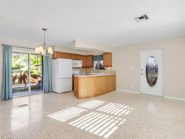 Open-concept living space with light-toned terrazzo flooring, a kitchen featuring wood cabinetry and white appliances, and a glass-paneled entry door