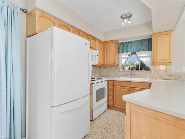 Kitchen featuring wood cabinetry, light-toned countertops, tile backsplash, and a built-in kitchen sink with a window overhead