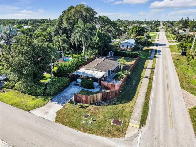 Aerial property view featuring a fence-enclosed front yard with mature landscaping and a concrete driveway