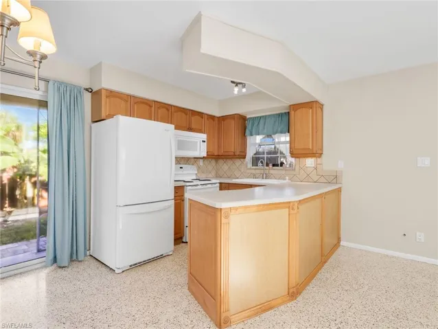 Kitchen featuring light wood cabinetry, white appliances, a tile backsplash, and a breakfast bar