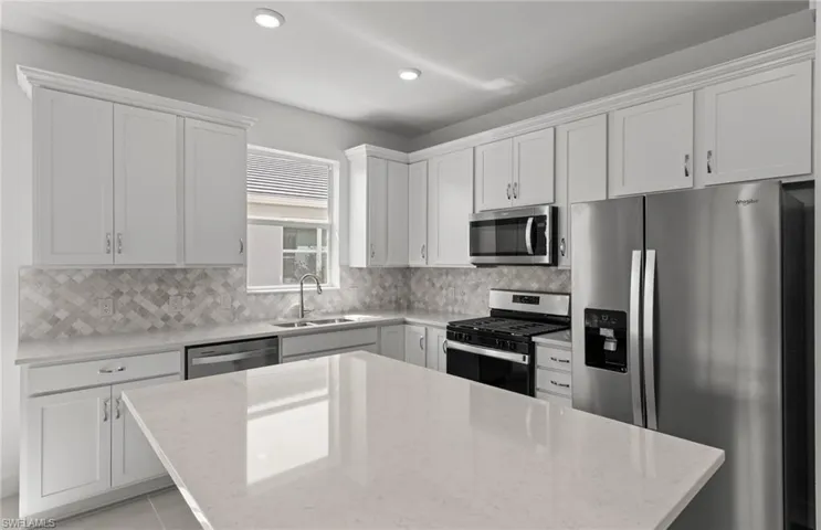 Kitchen with stainless steel appliances, light stone counters, backsplash, sink, and white cabinets