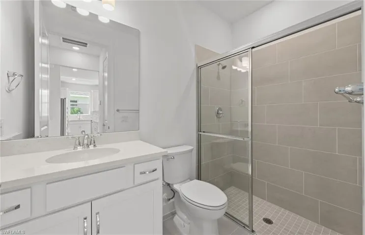 Bathroom featuring a shower with door, toilet, and vanity