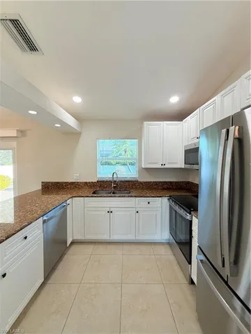 Kitchen featuring white cabinetry, refrigerator, stainless steel range, dark stone counters, and recessed lighting