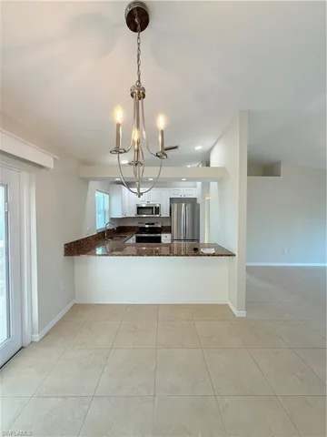 Kitchen featuring dark stone counters, decorative light fixtures, stainless steel appliances, a peninsula, and white cabinetry