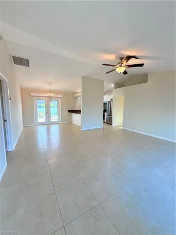 Unfurnished room featuring a chandelier, ceiling fan, vaulted ceiling, and light tile patterned flooring