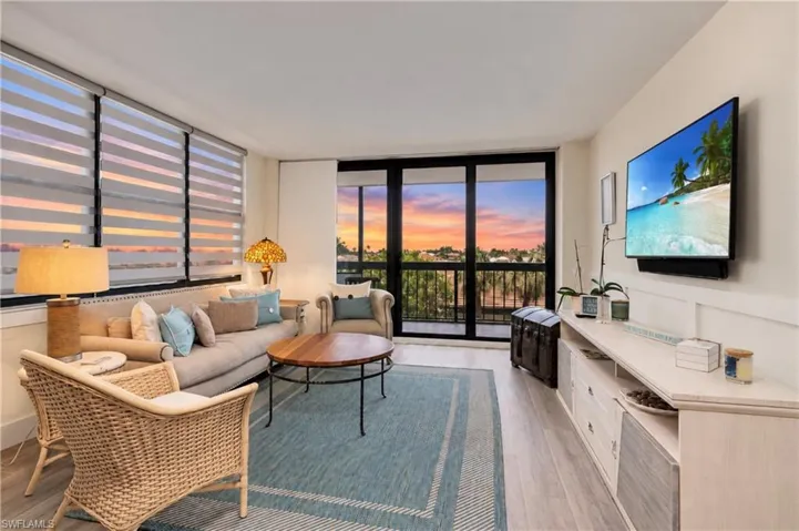 Living area featuring large windows with adjustable shades, wood-finish flooring, and sliding glass doors leading to a private balcony