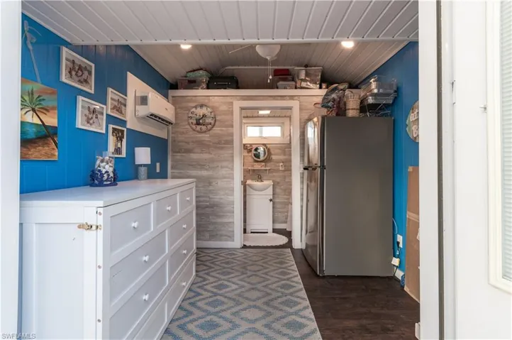 Kitchen featuring freestanding refrigerator, wooden walls, light countertops, dark wood-style floors, and white cabinetry