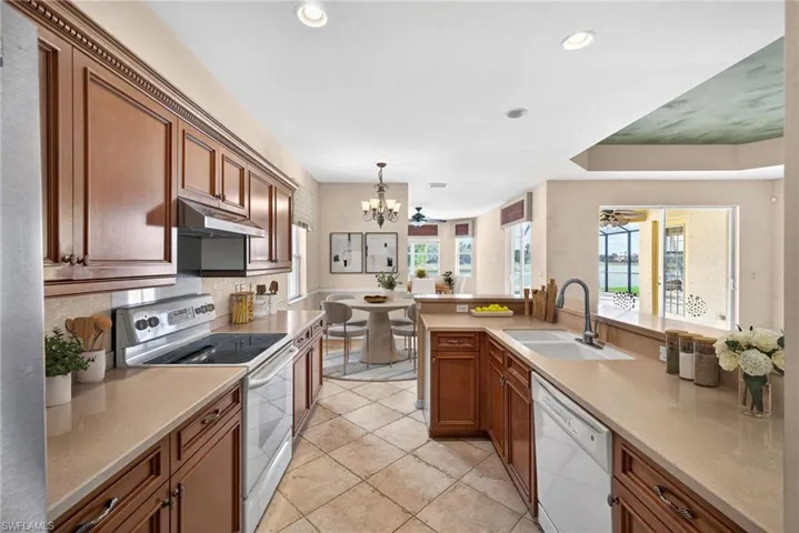 Kitchen featuring white appliances, wood finish cabinets, suspended lighting, a peninsula, and light stone counters