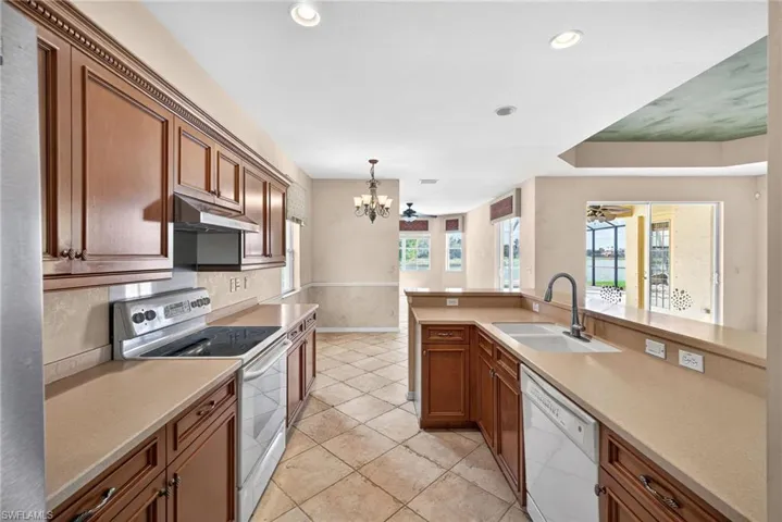 Kitchen featuring white appliances, wood finish cabinetry, a chandelier, and a ceiling fan